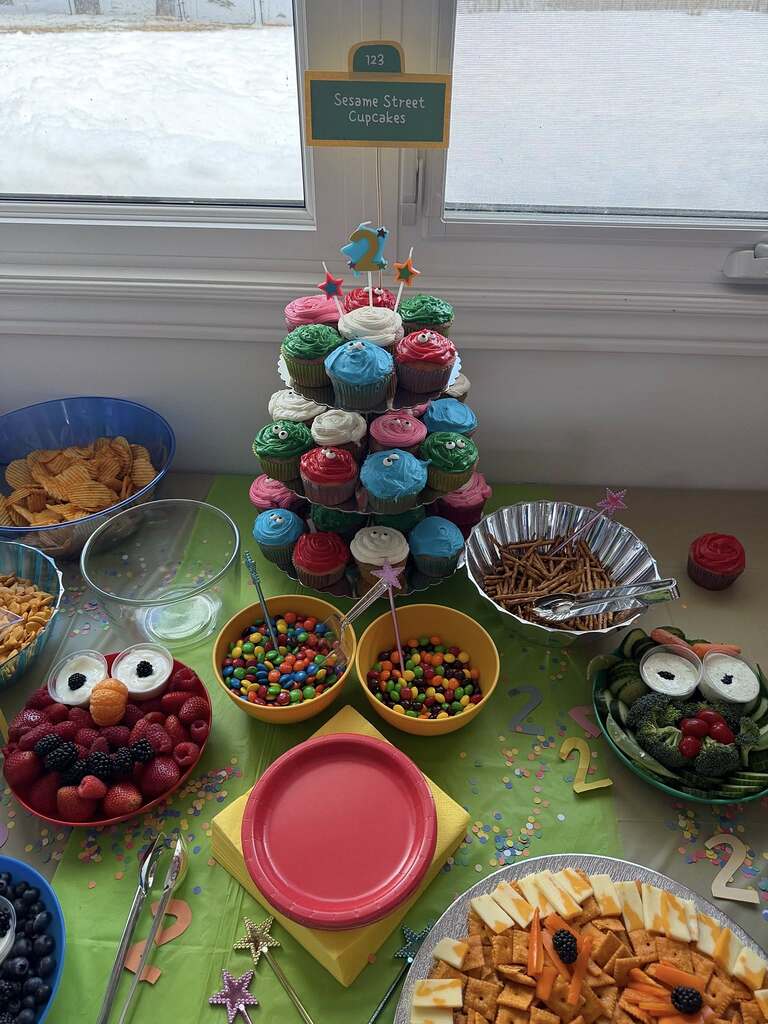 Sesame Street birthday party snack table with colorful cupcakes, fruit platter, candy, and cheese and cracker tray.