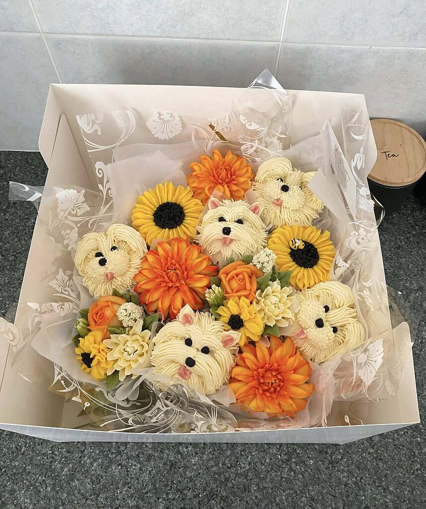 Cupcake bouquet featuring buttercream Westie dogs, sunflowers, and orange dahlias in a gift box.