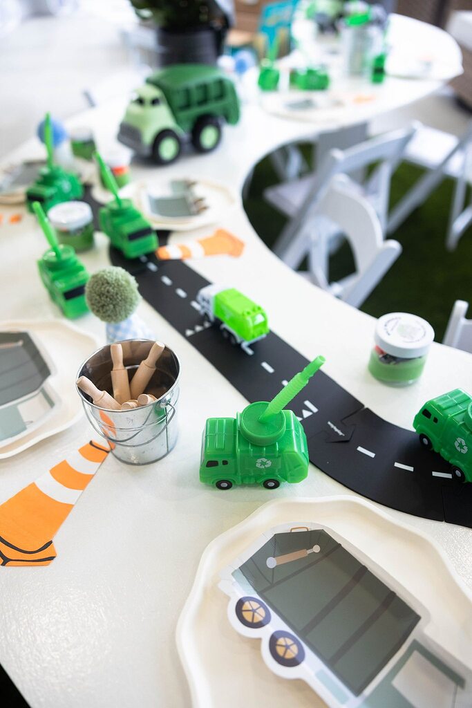Table setting with green recycling truck themed party decorations, road track, and construction cone napkins.
