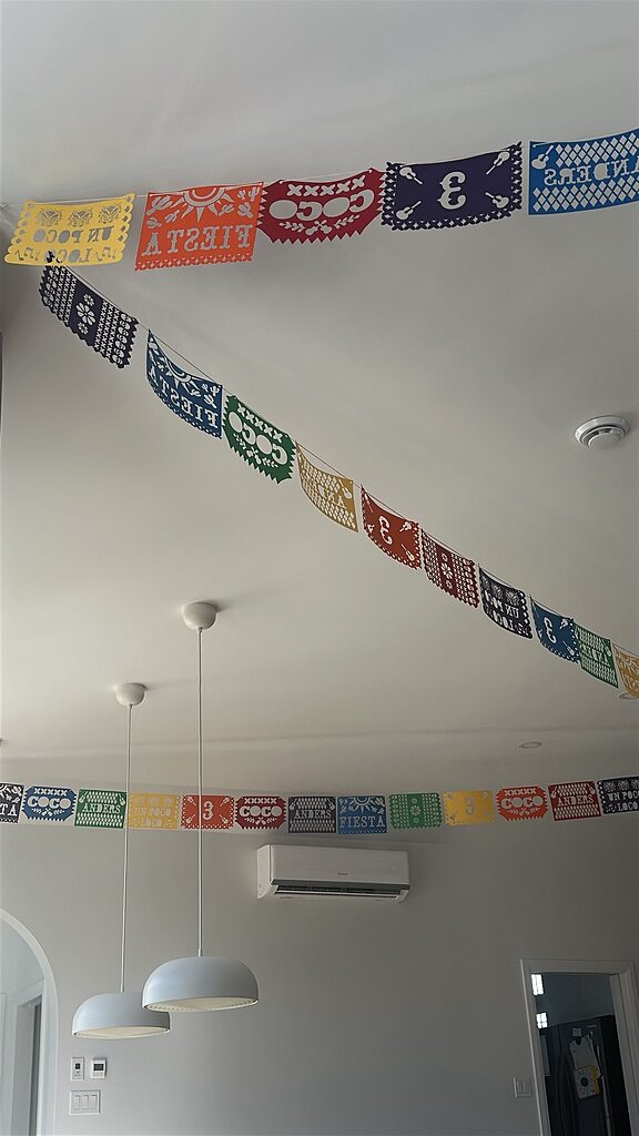 Colorful Coco-themed Mexican paper banner hanging on a white ceiling.