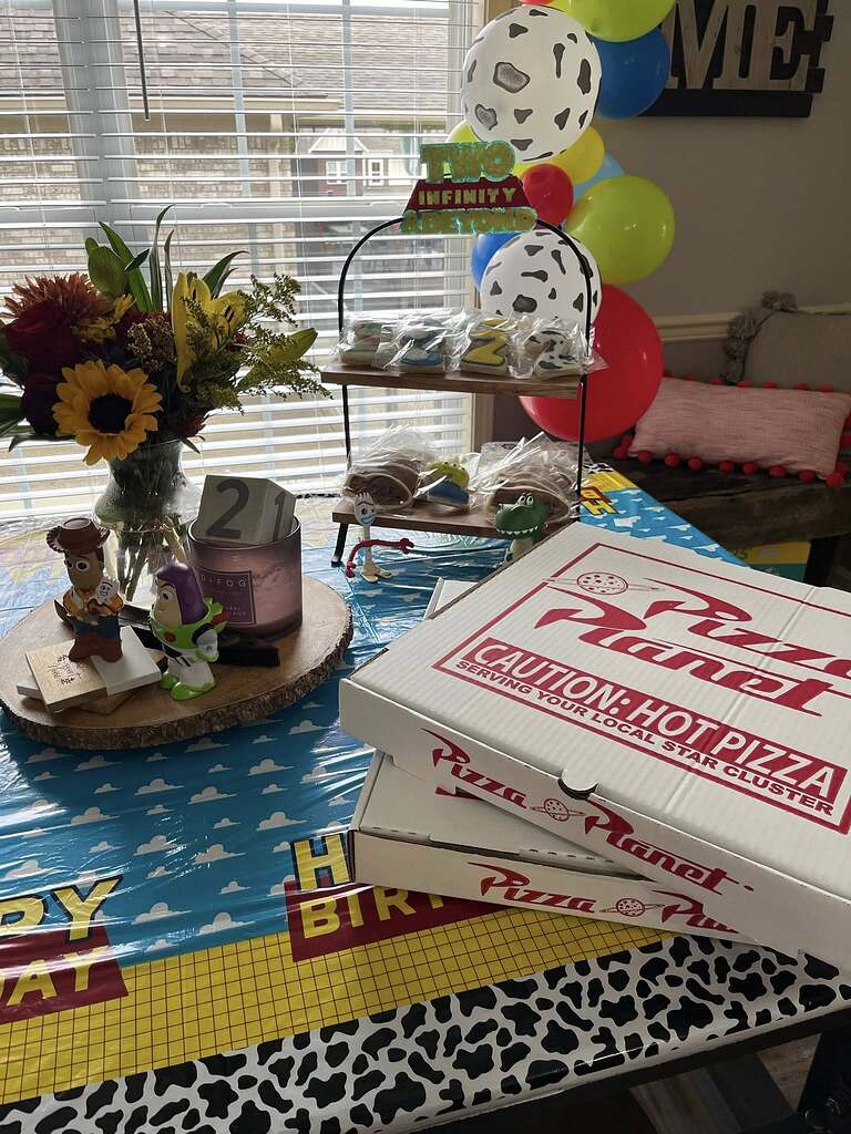 Toy Story themed birthday tabletop with Pizza Planet pizza boxes and character figurines.