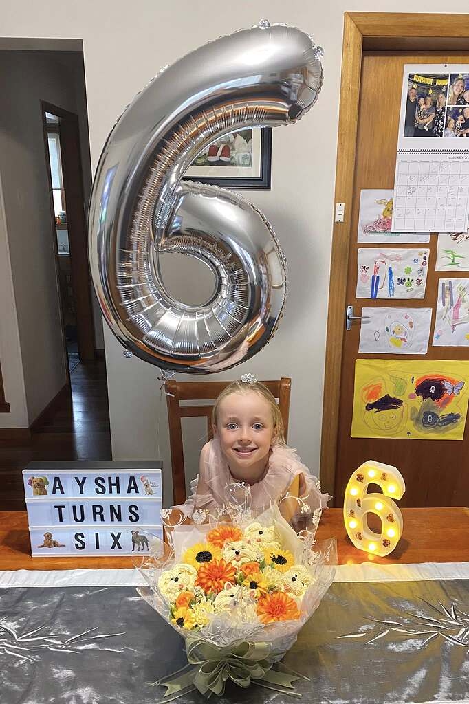 Young girl celebrating her sixth birthday with a large silver number balloon, light-up sign, and cupcake bouquet.
