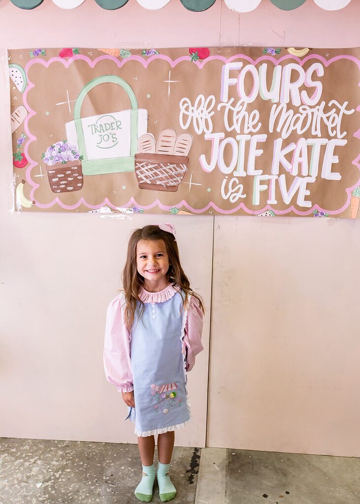 Young girl smiling in front of a Trader Joe's themed birthday banner.