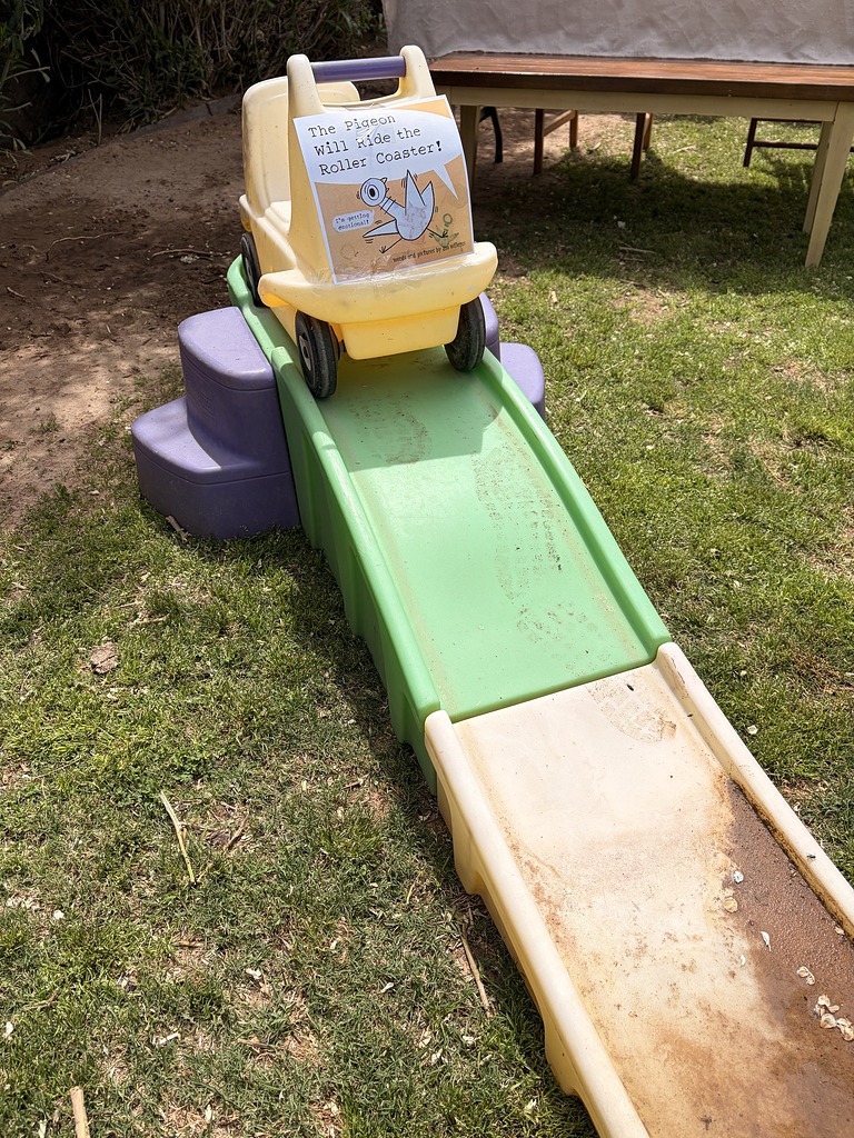 Toy car with a The Pigeon Will Ride the Roller Coaster! book cover taped to it at the top of a plastic slide.