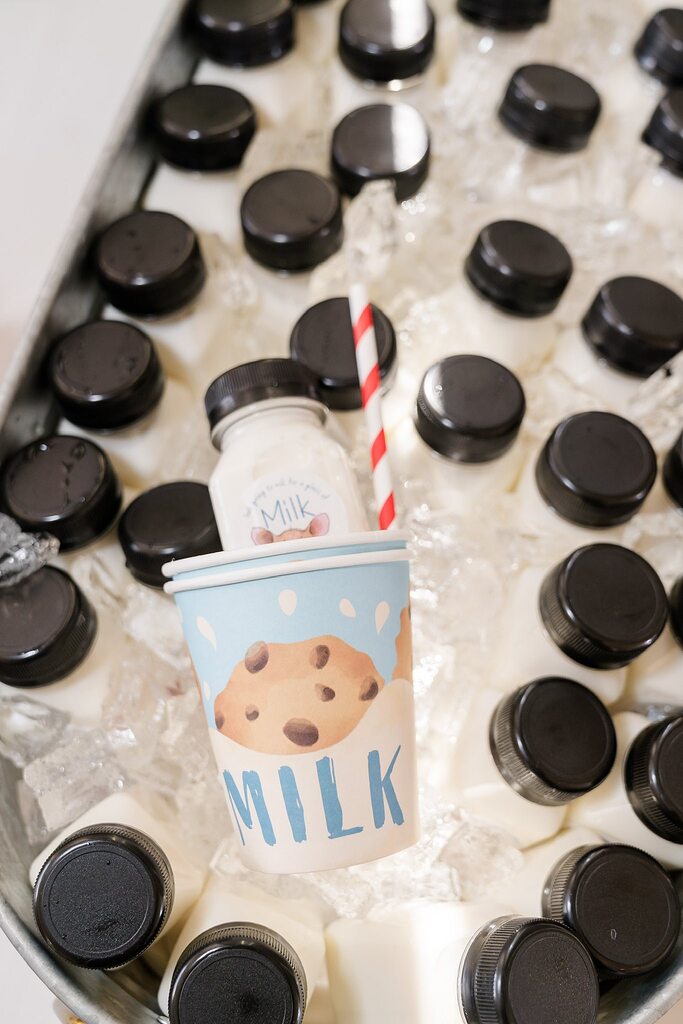 Small bottles of milk on ice with a decorative paper cup featuring a chocolate chip cookie design
