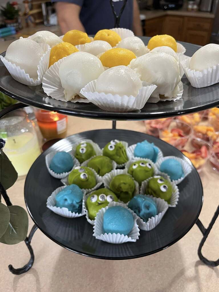 Two-tiered tray serving white and yellow cake pops on the top level and alien-themed green and blue cake pops on the bottom level.