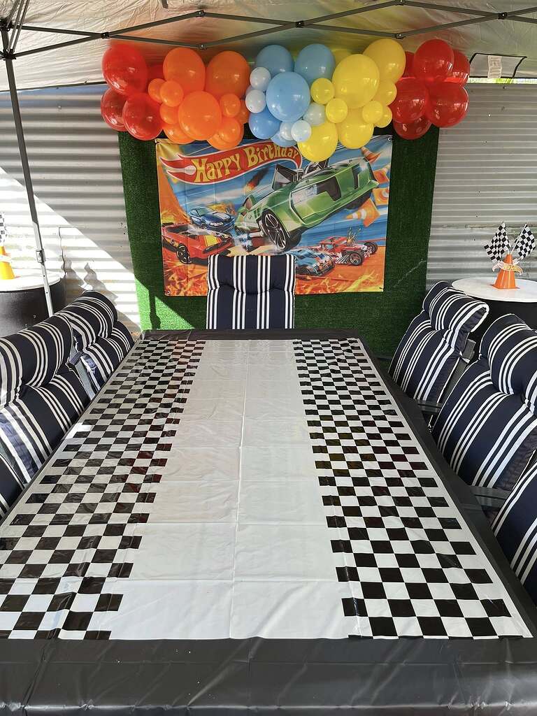 Hot Wheels themed birthday party setup with a checkered tablecloth and colorful balloon arch backdrop.