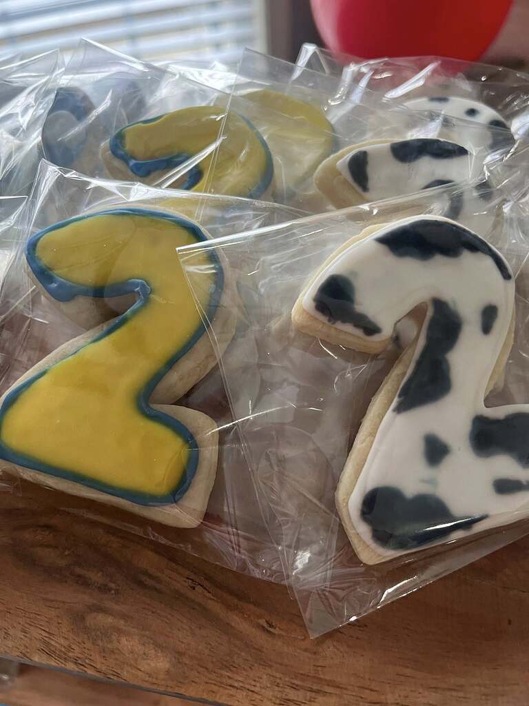 Individually wrapped sugar cookies shaped like the number two, featuring yellow and cow-print icing designs.
