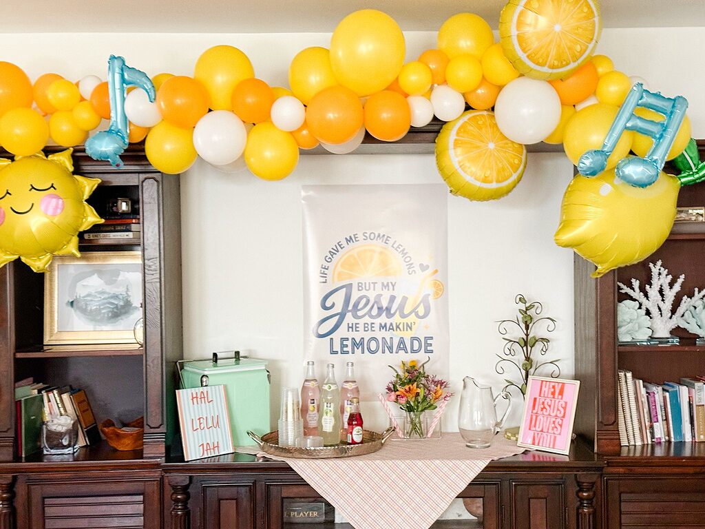 Lemonade party decor featuring yellow balloons, lemon-shaped Mylar balloons, and a spiritual-themed poster.