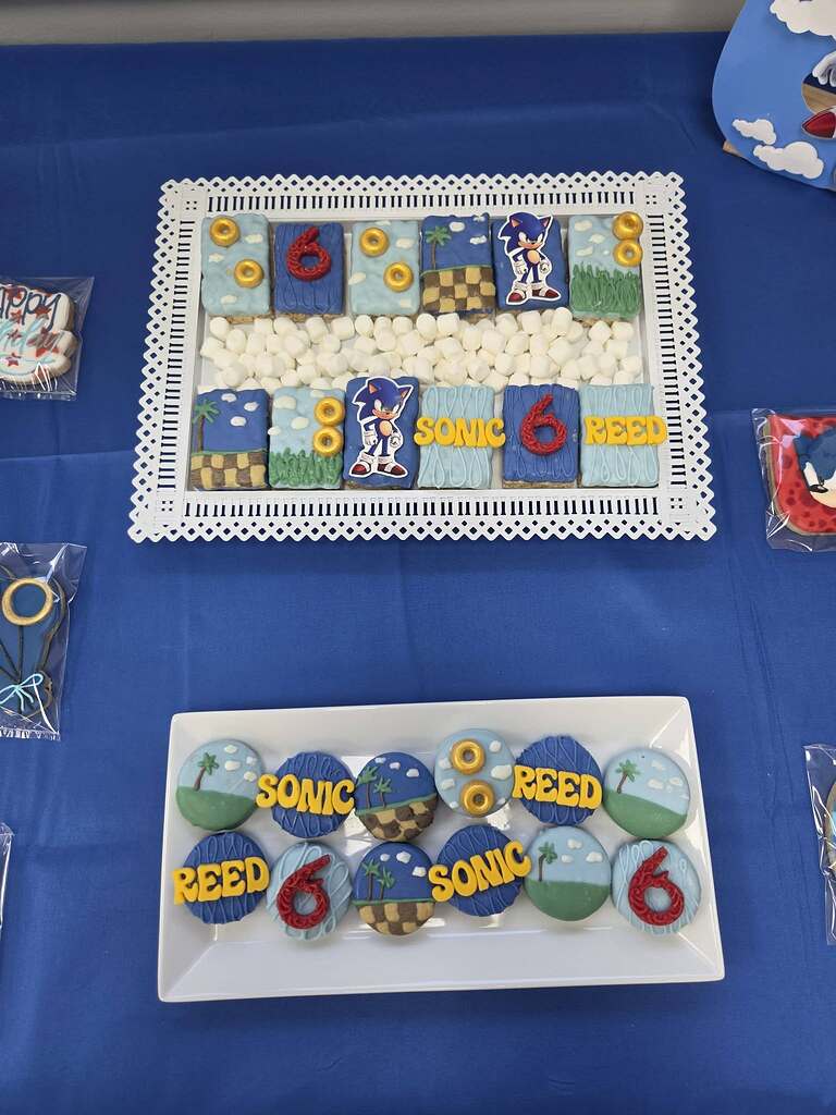 Table display of custom decorated Sonic the Hedgehog themed cookies and rice krispies for a 6th birthday party.