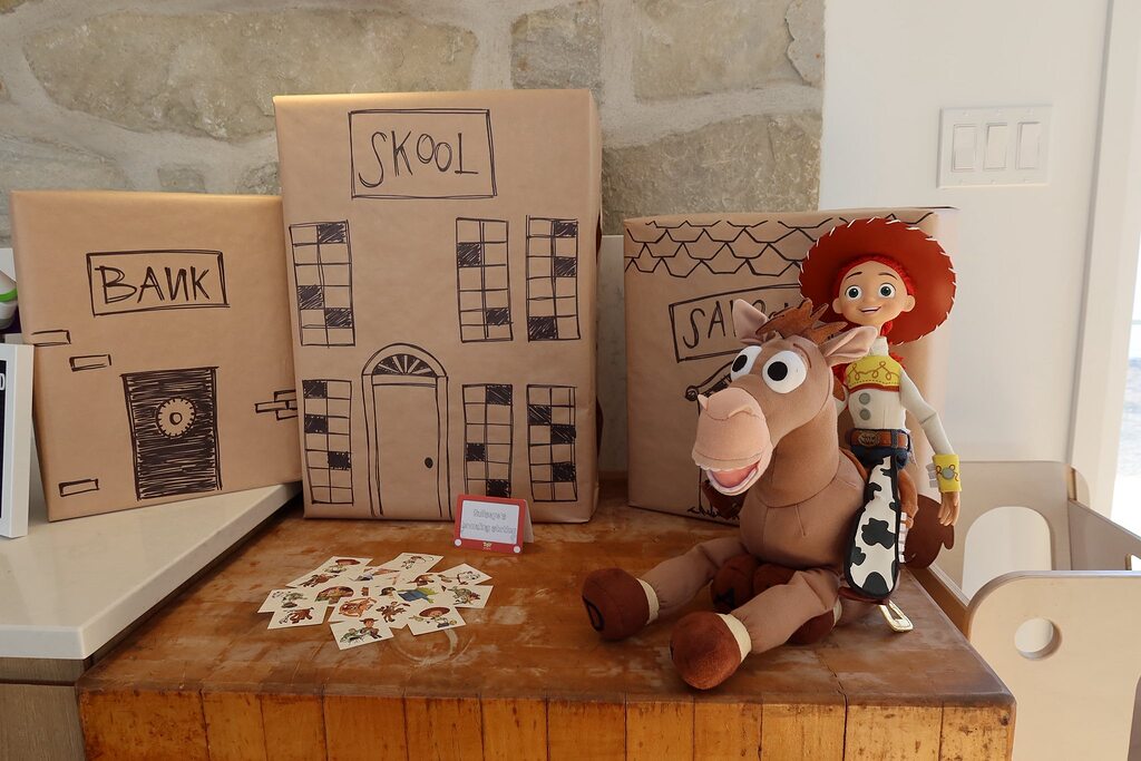 Jessie and Bullseye plush toys in front of cardboard box buildings labeled Skool, Bank, and Saloon.