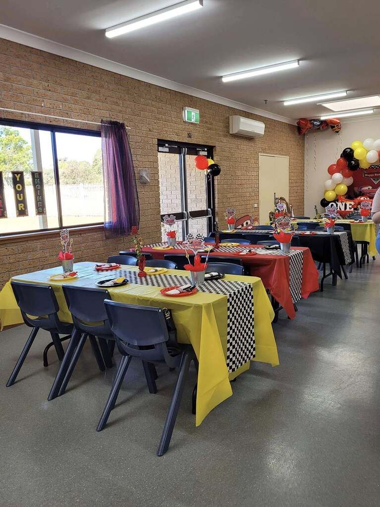 Race car themed party tables with yellow and red tablecloths, black checkerboard runners, and matching centerpieces.