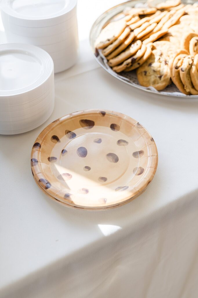 Paper plates decorated with a chocolate chip cookie pattern next to a platter of real cookies