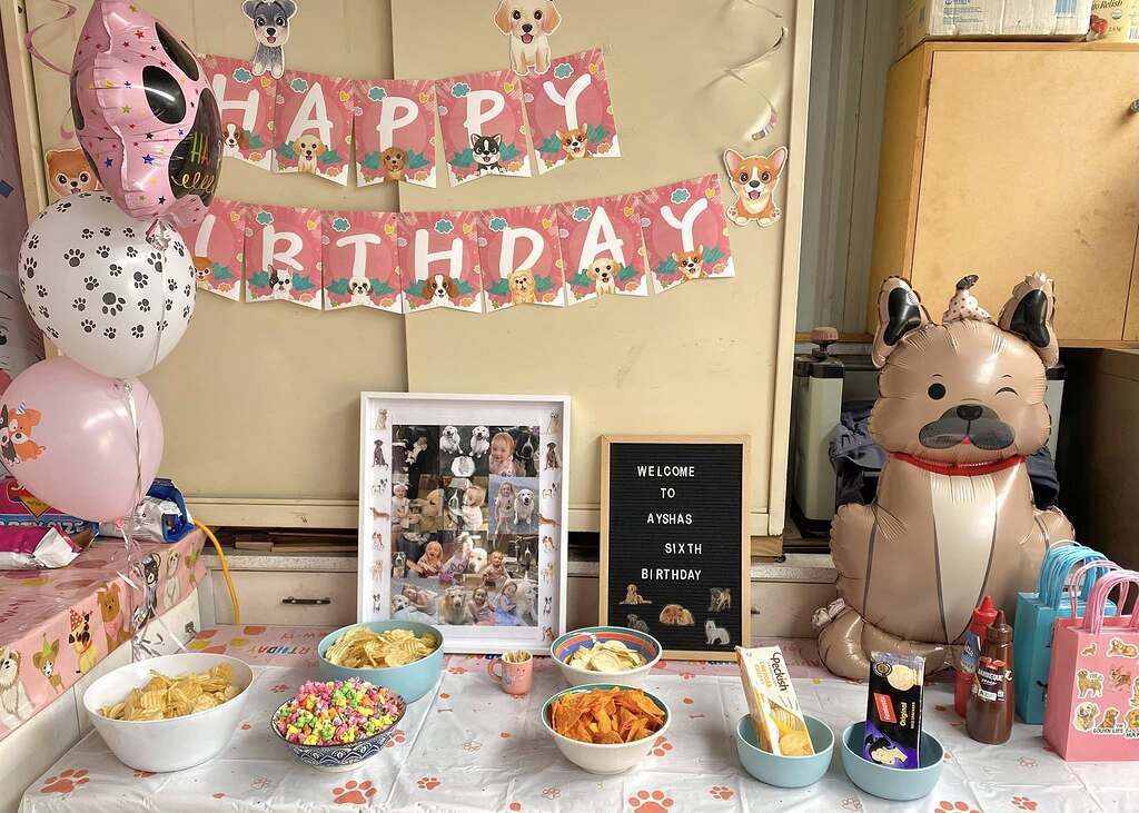 Puppy-themed birthday party decorations with a Happy Birthday banner, dog balloons, snacks, and a photo collage.