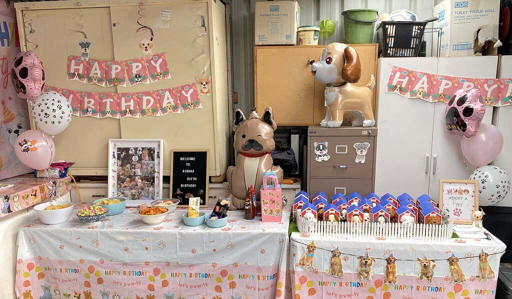 Puppy-themed birthday party decorations with balloons, photo frame, snacks, and toy dog houses on tables.