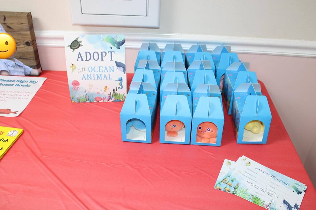 Adopt an ocean animal station at a party with blue treat boxes containing plush toys and adoption certificates.