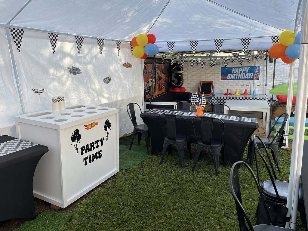 Hot Wheels themed outdoor birthday party setup with black table covers, checkered flags, and party decorations.