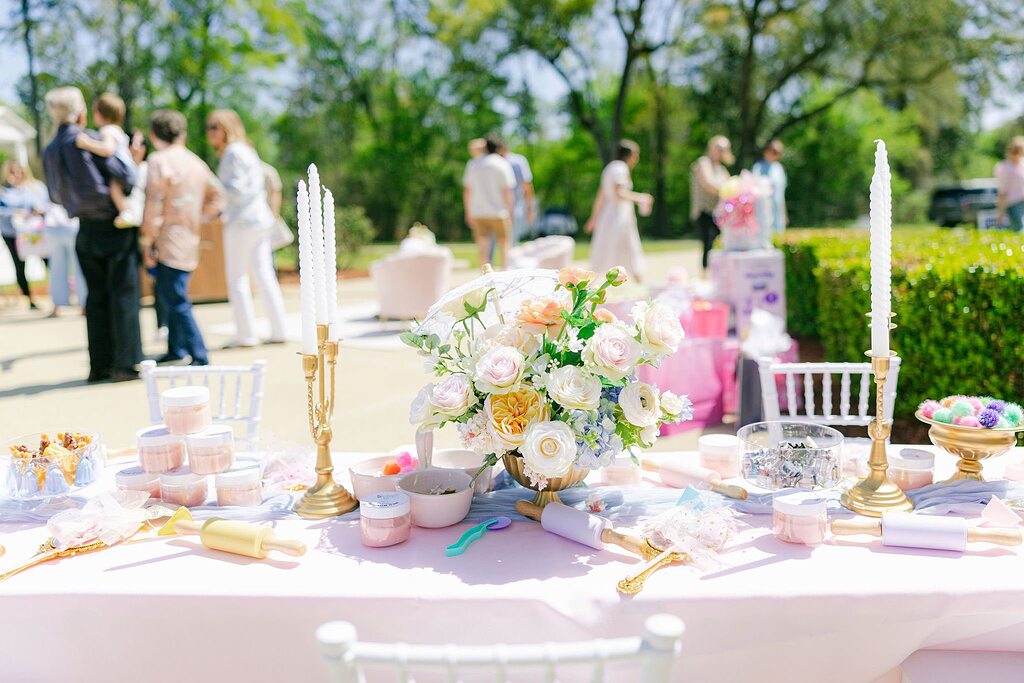 Outdoor party table set with pastel florals, gold candlesticks, and decorative rolling pins for an event.