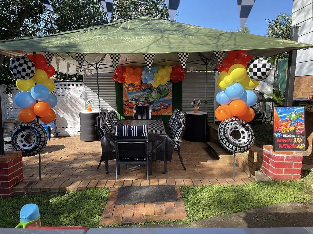 Outdoor patio decorated for a Hot Wheels themed 3rd birthday party with racing tire balloons and checkered flags.