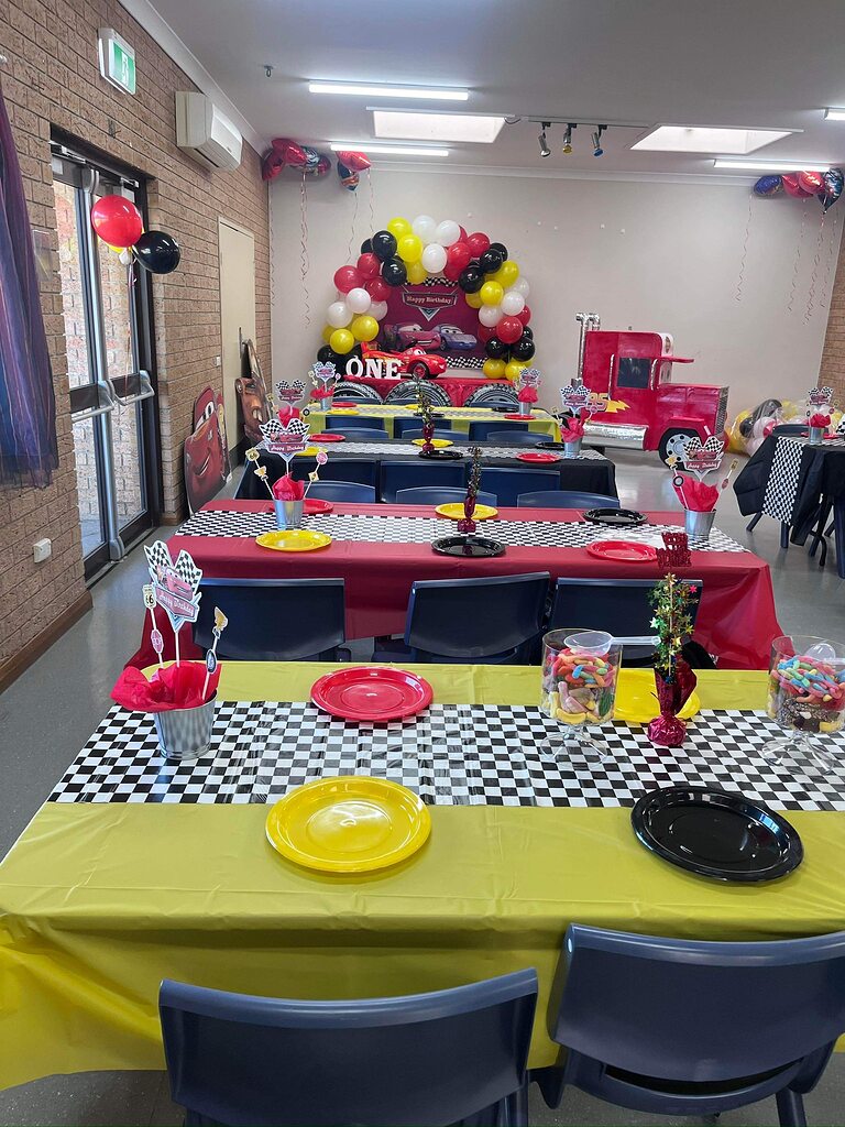 Dining hall decorated for a Cars-themed birthday party with red, yellow, and black checkered table settings.