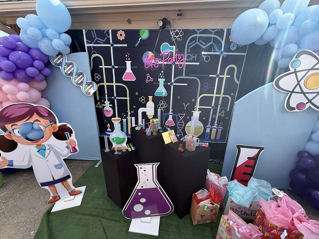 Science themed birthday party decorations featuring a lab backdrop, balloon arches, and cutout scientist figures.