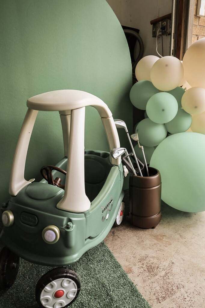Personalized green toy car with golf clubs in a stand next to pastel party balloons