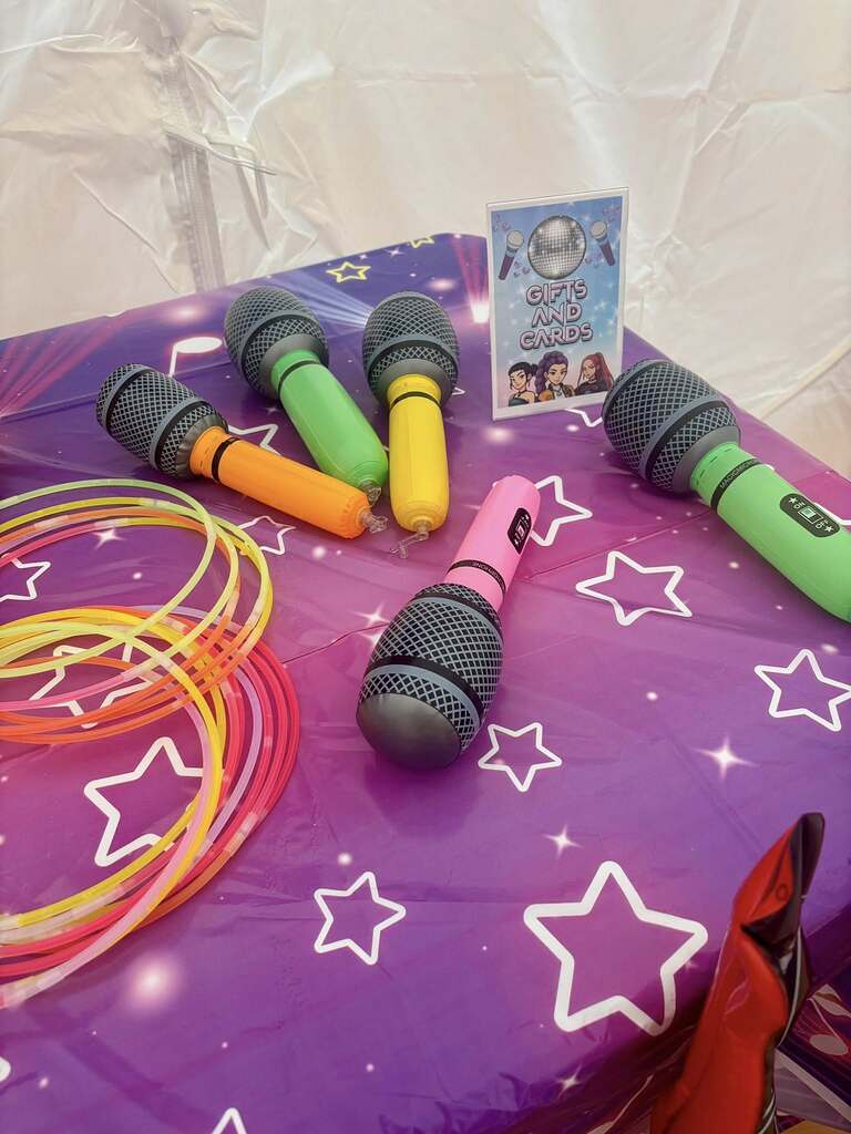 Colorful inflatable toy microphones and glow sticks on a purple star-patterned table with a Gifts and Cards sign.