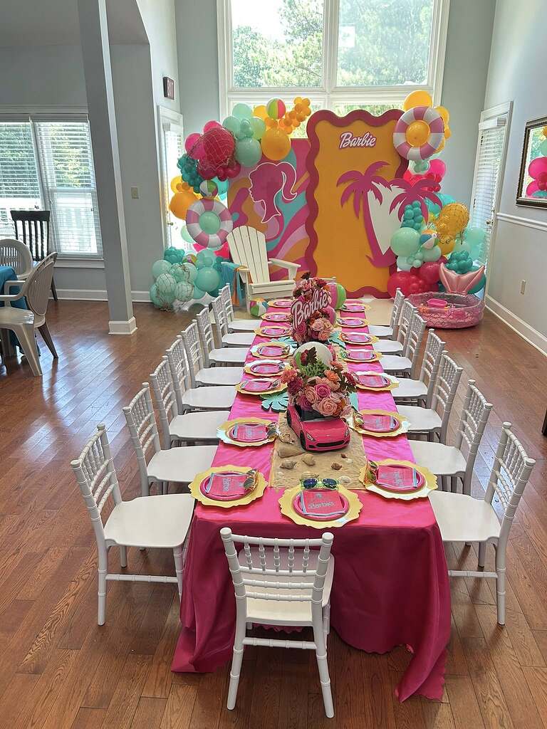 Table set for a Barbie themed party with pink tablecloth, floral centerpieces in toy cars, and colorful balloons.