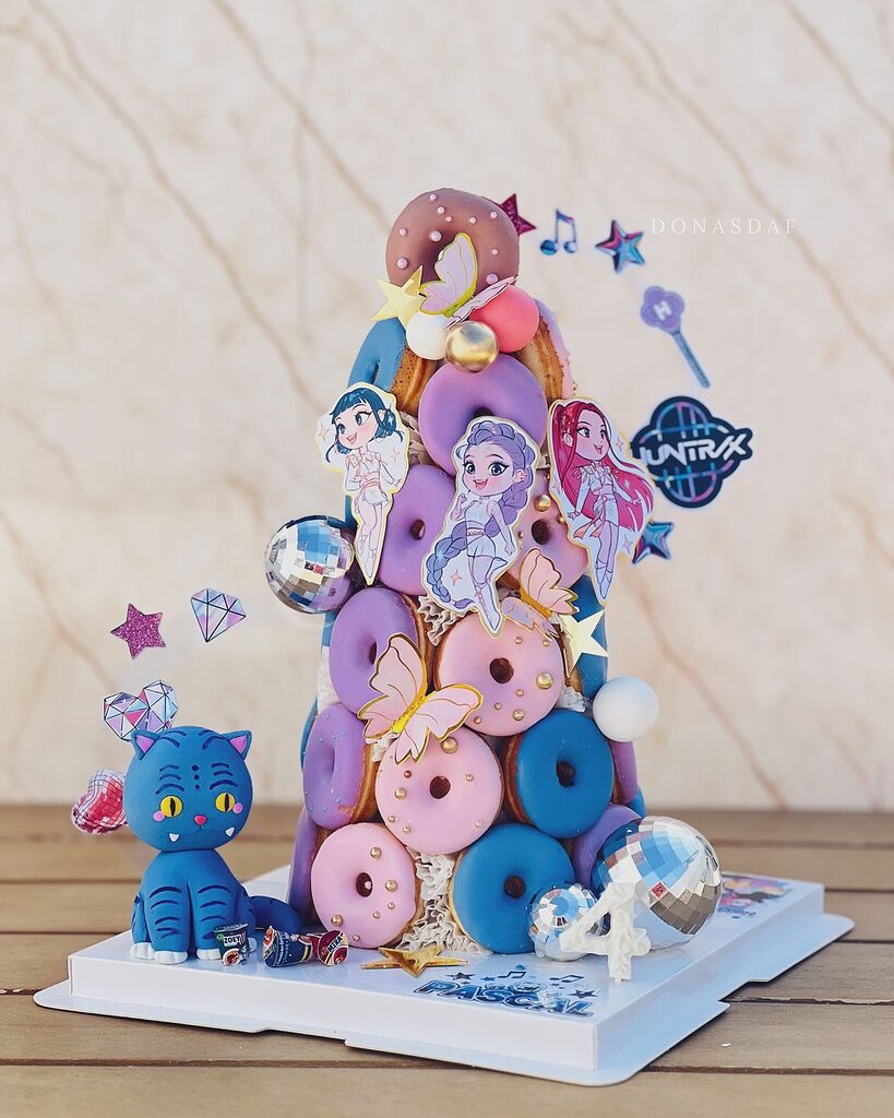 Tiered donut tower cake decorated with cartoon character cutouts, stars, butterflies, and a blue cat figure.