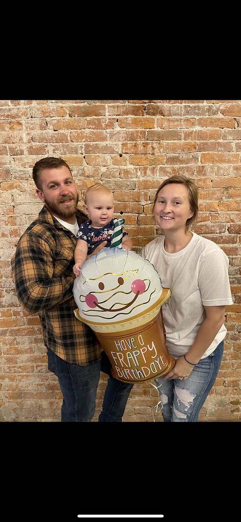 Family of three posing with a milkshake-shaped balloon that says Have a Frappy Birthday