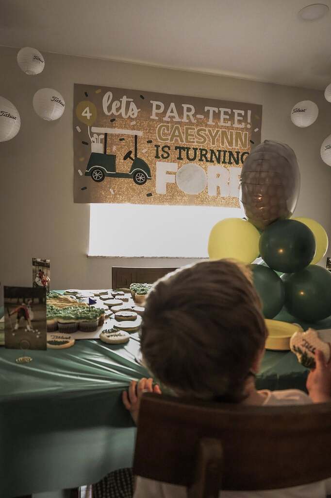 Child sitting at a golf-themed fourth birthday party with a banner reading Lets Par-Tee Caenynn is Turning Fore