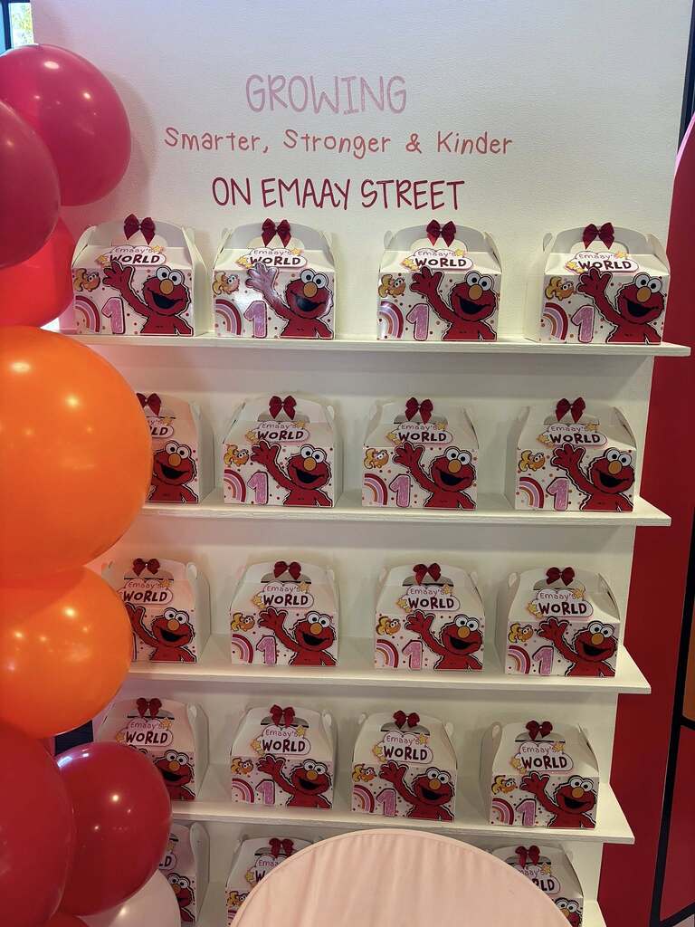 Shelves filled with Elmo themed party favor gift boxes decorated with red bows for a first birthday celebration.