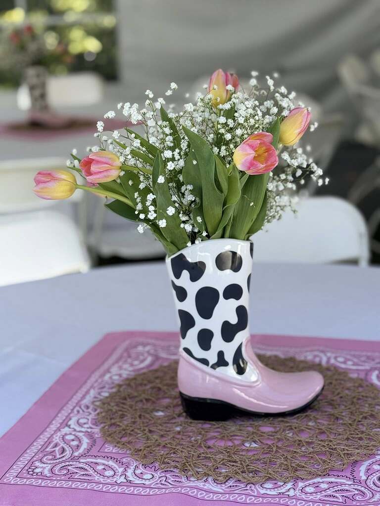 Ceramic cowboy boot vase with cow print and pink accents filled with pink tulips and baby's breath.