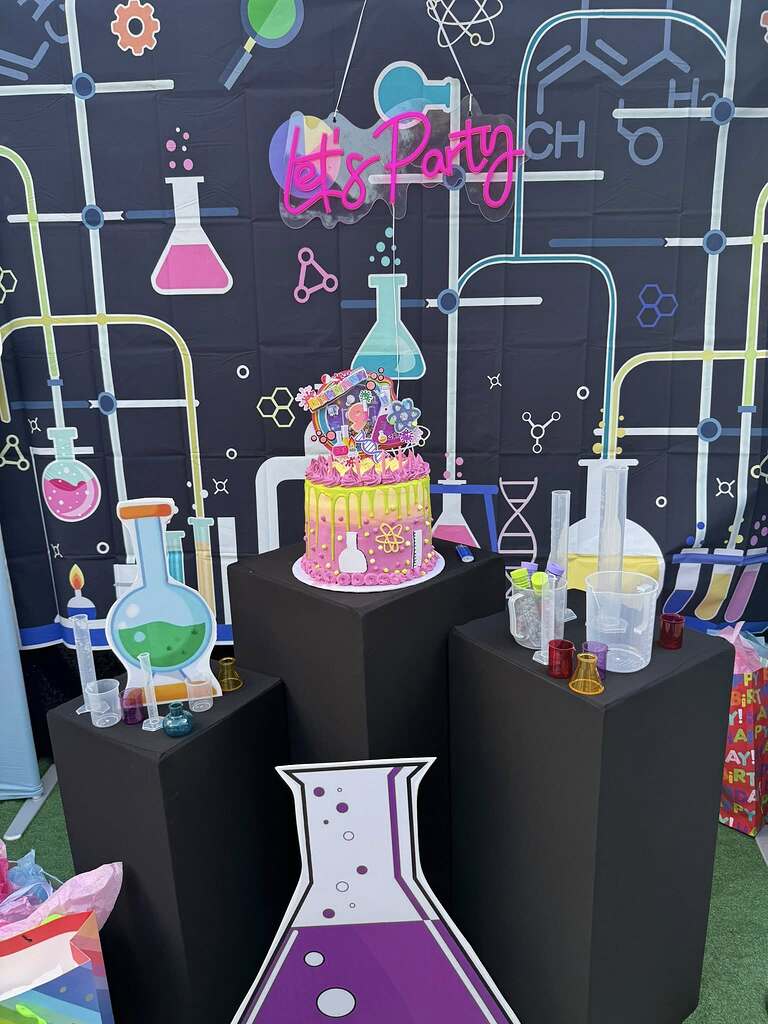Science-themed birthday party setup with a decorated cake, lab beakers, and a chemical experiment backdrop.