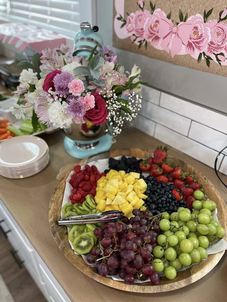 Large wooden platter filled with fresh assorted fruit including pineapple, grapes, berries, and kiwi slices.