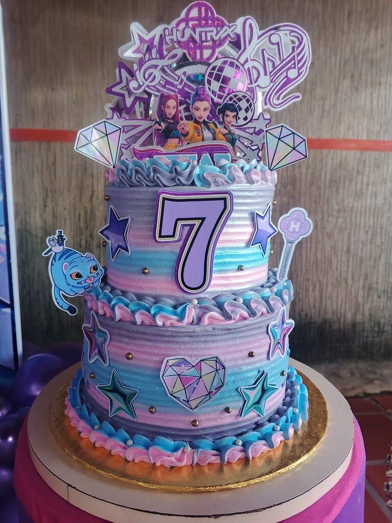 Two-tier purple and blue ombre birthday cake decorated with K-pop themed toppers and a large number 7.