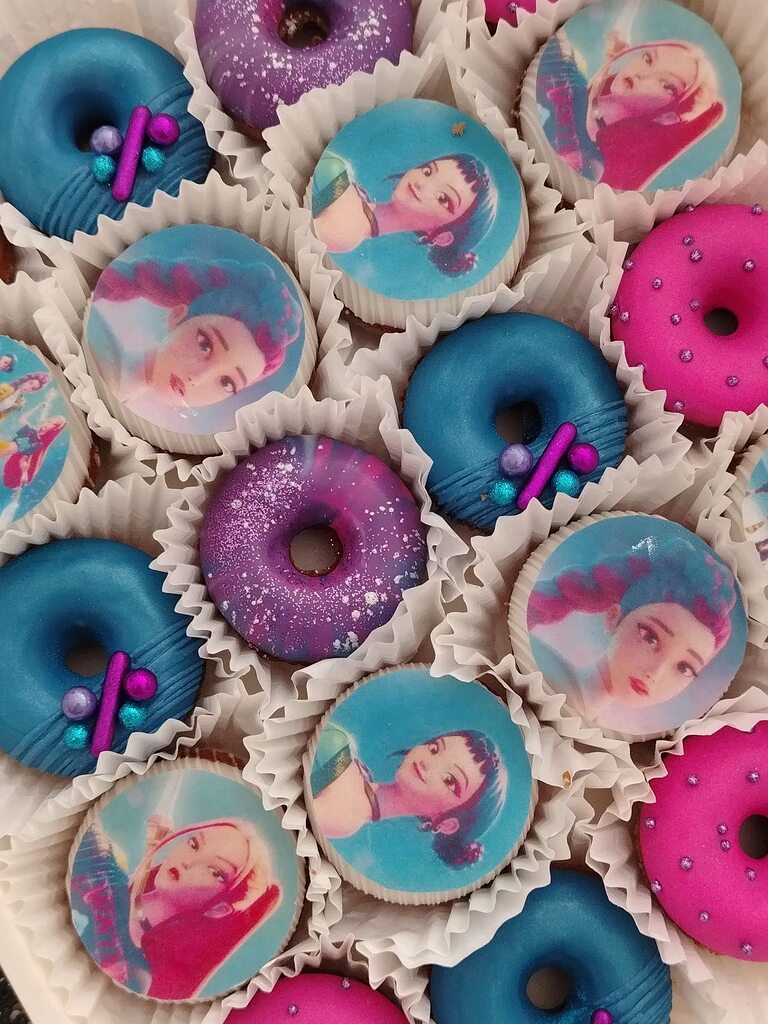 Assorted gourmet donuts featuring character images, metallic blue glaze, and glittery purple icing in a box