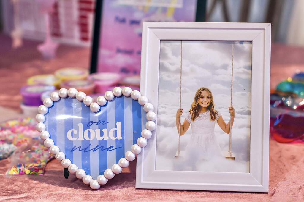Table centerpiece featuring a white-framed photo of a girl on a swing and a heart-shaped sign saying On Cloud Nine