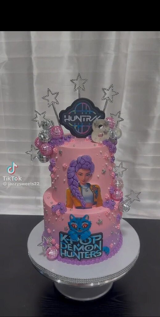 Two-tier pink K-Pop Demon Hunters birthday cake decorated with disco balls and stars.