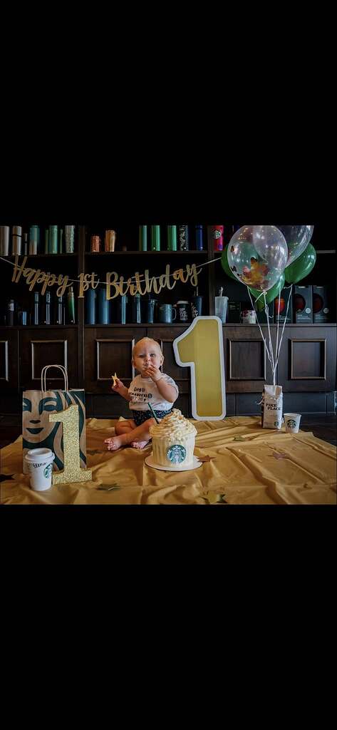 Baby celebrating first birthday with Starbucks-themed decorations, balloons, and cake