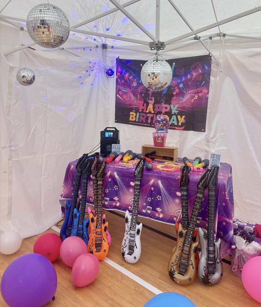 Rock and roll themed birthday party setup with inflatable toy guitars, disco balls, and karaoke machine.