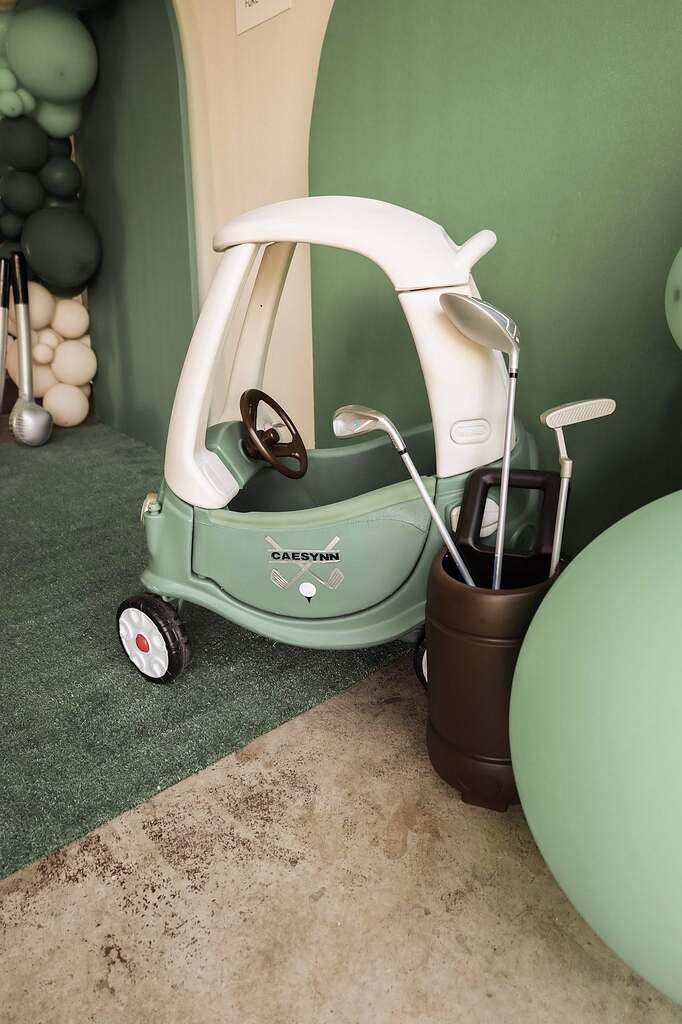 Customized green toddler ride-on car with golf clubs, decorated for a sports-themed party.