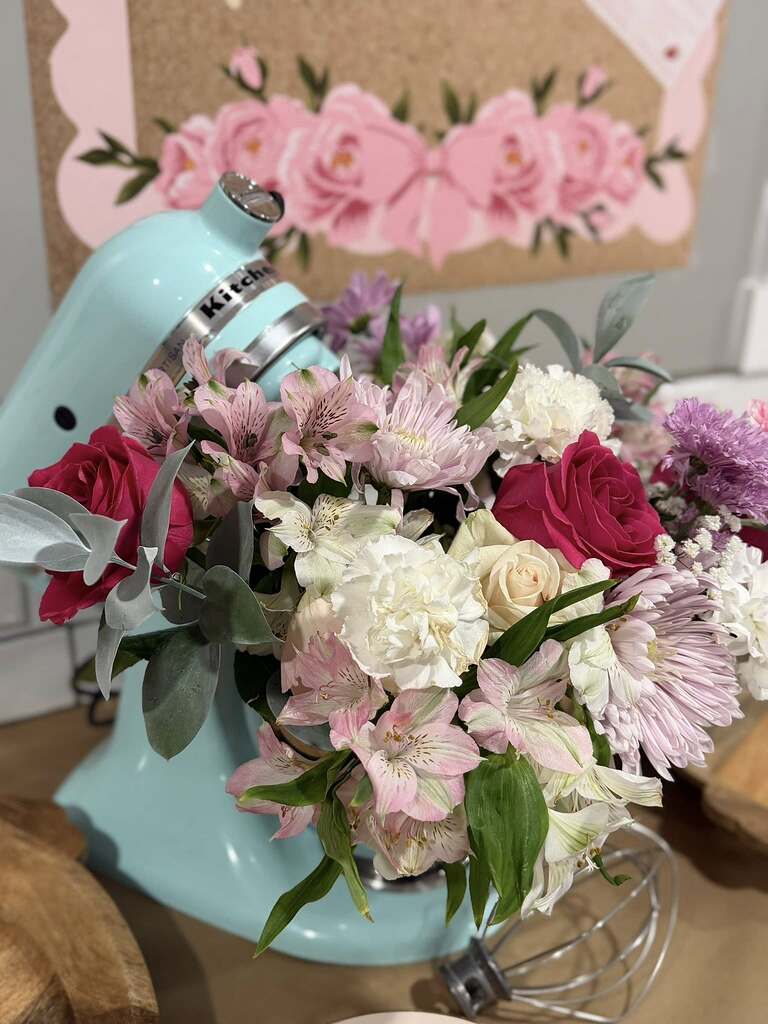 Light blue stand mixer filled with a vibrant bouquet of pink roses, white carnations, and alstroemeria flowers.