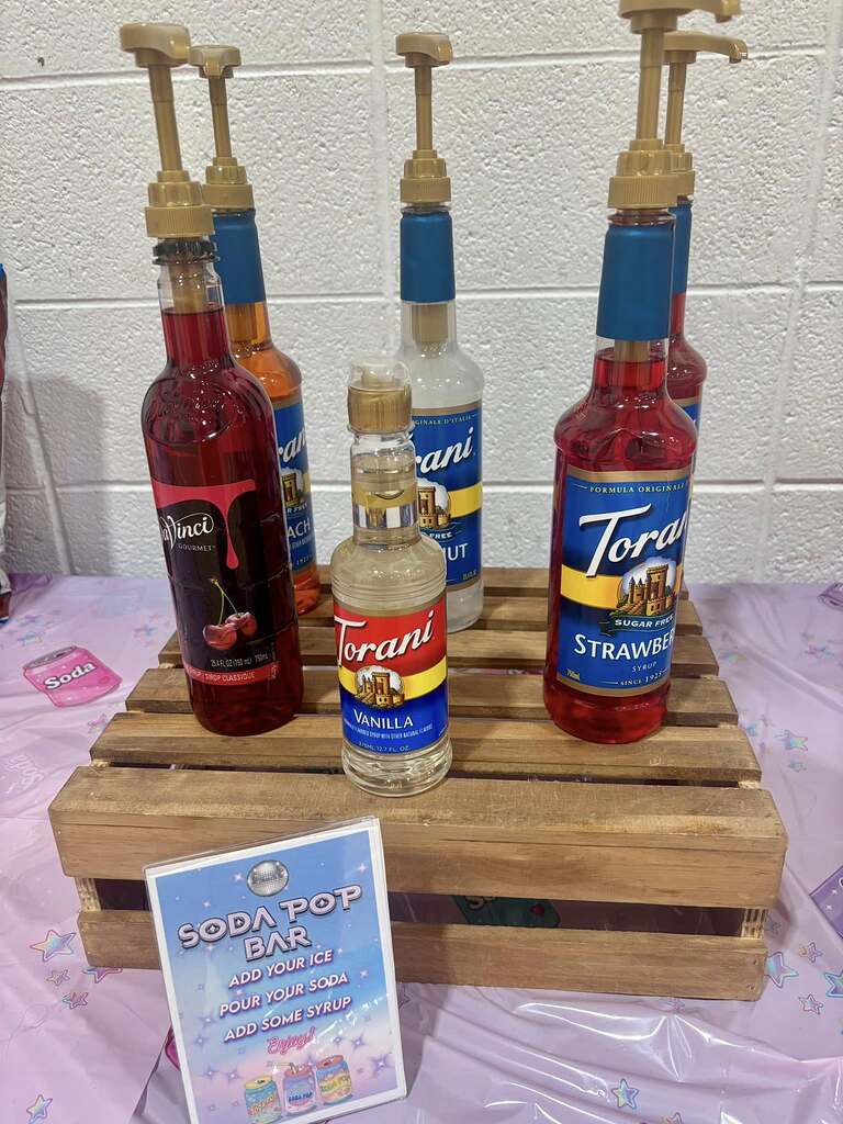 Assorted Torani and DaVinci syrup bottles with pumps on a wooden crate for a DIY soda pop bar.