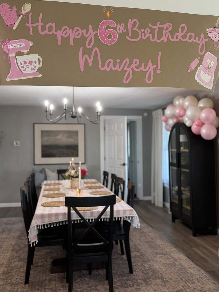 Dining room decorated for a 6th birthday with a pink baking-themed banner hanging in the foreground.