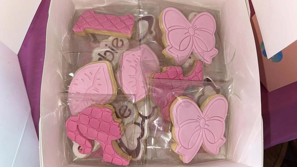 Box of assorted pink iced sugar cookies in shapes including bows and doll silhouettes.