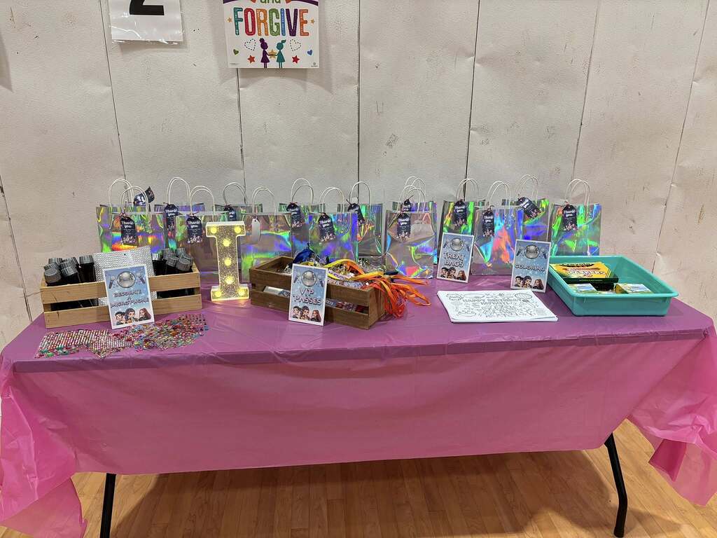Table arranged with colorful treat bags, microphone decoration supplies, and activity stations for a party.