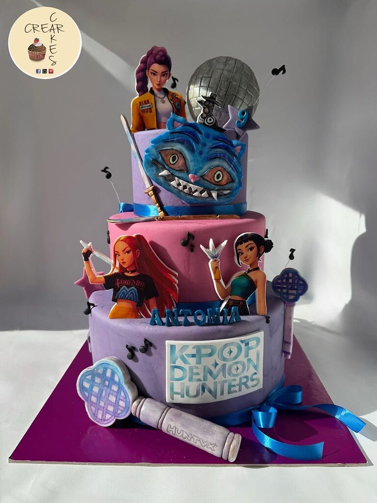 Three-tiered K-Pop Demon Hunters themed birthday cake decorated with character cutouts, music notes, and a disco ball.