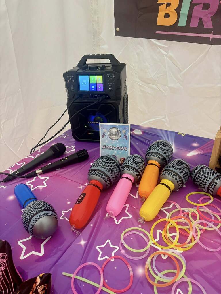 Karaoke machine with multiple colorful toy microphones and glow sticks spread on a purple star-patterned table.