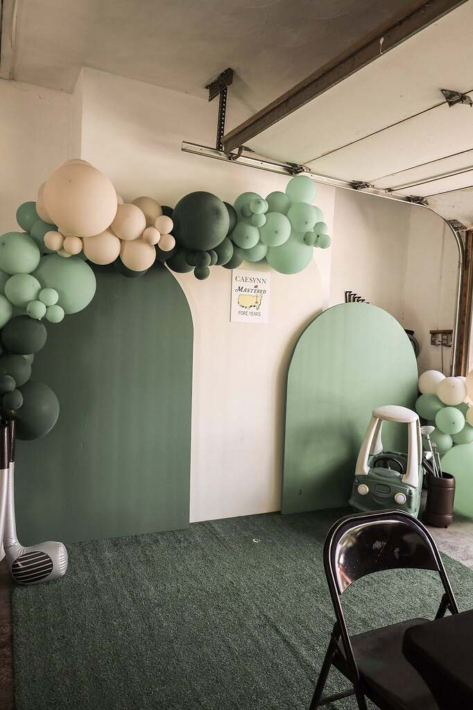 Golf-themed party backdrop with arched green panels, green and cream balloon garland, and decorative party supplies.